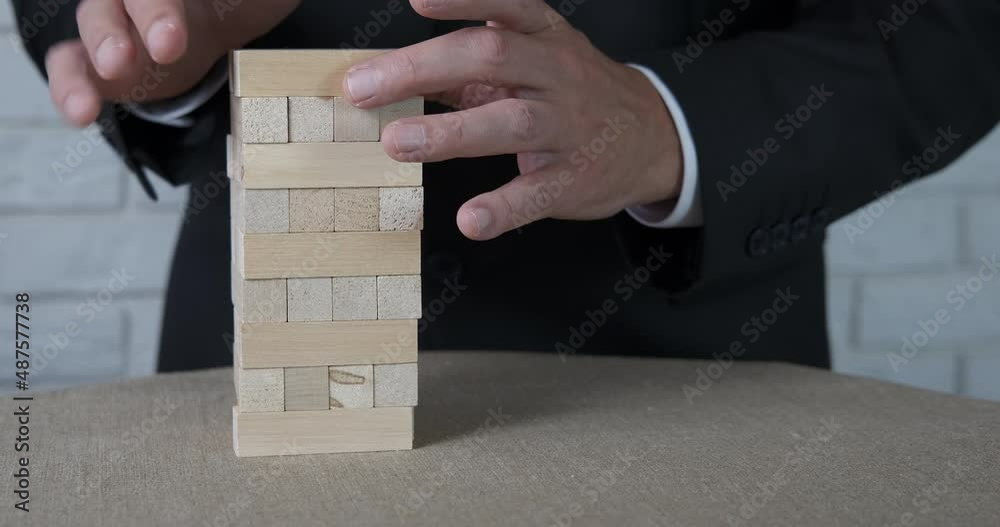 Make a small block tower. A businessman makes a wooden tower from bricks in the office. Make a small block tower. A businessman makes a wooden tower from bricks in the office.