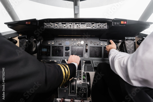 cropped view of pilots using yoke and thrust lever in airplane simulator.