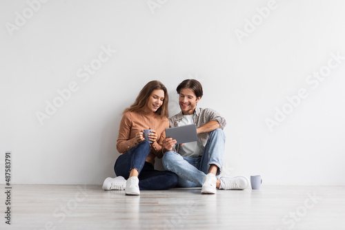 Satisfied millennial caucasian family planning future home interior with tablet, sit on floor