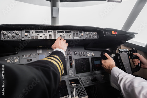 cropped view of pilot reaching control panel near co-pilot using yoke in airplane simulator. photo