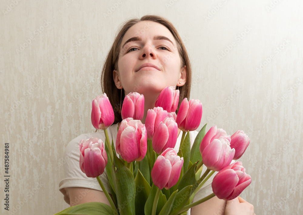 Womans day concept: Young woman holds pack of tulips near her face while enjoying herself Womans day concept: Young woman holds pack of tulips near her face while enjoying herself
