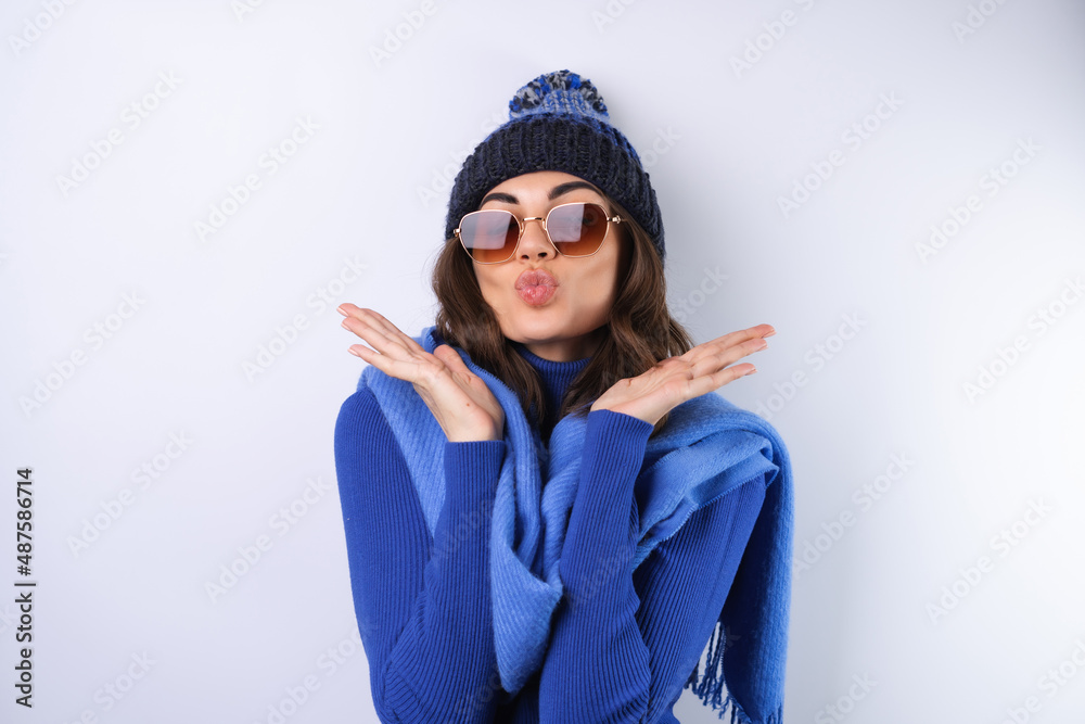 Young woman in a blue golf turtleneck, hat and scarf, sunglasses, on a white background, cheerful in a good mood Young woman in a blue golf turtleneck, hat and scarf, sunglasses, on a white background, cheerful in a good mood