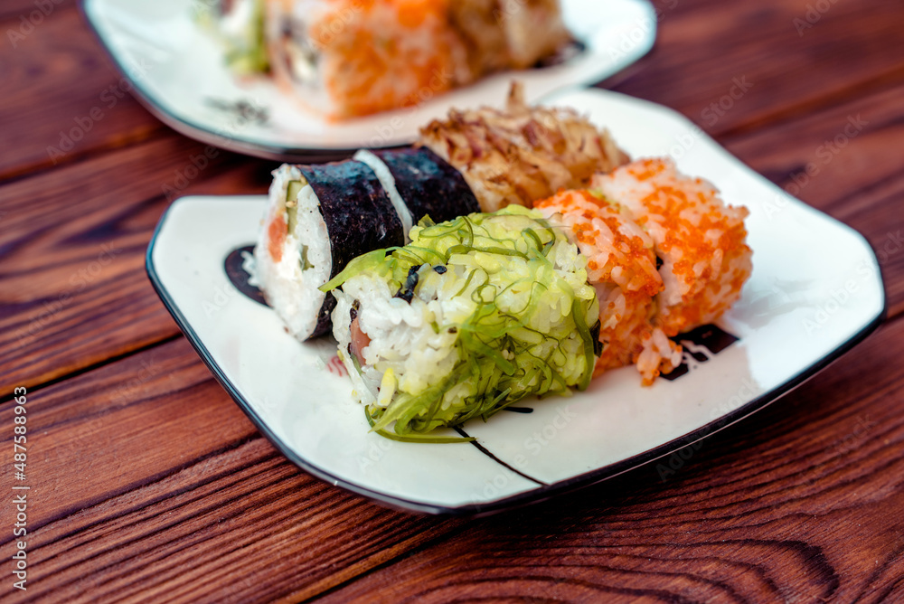 Several sushi on a white plate standing on a brown wooden background
Several sushi on a white plate standing on a brown wooden background