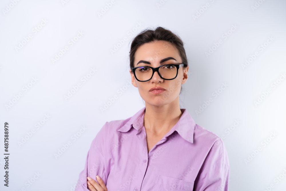 Young woman in a lilac shirt on a white background in glasses for vision looks angrily at the camera Young woman in a lilac shirt on a white background in glasses for vision looks angrily at the camera