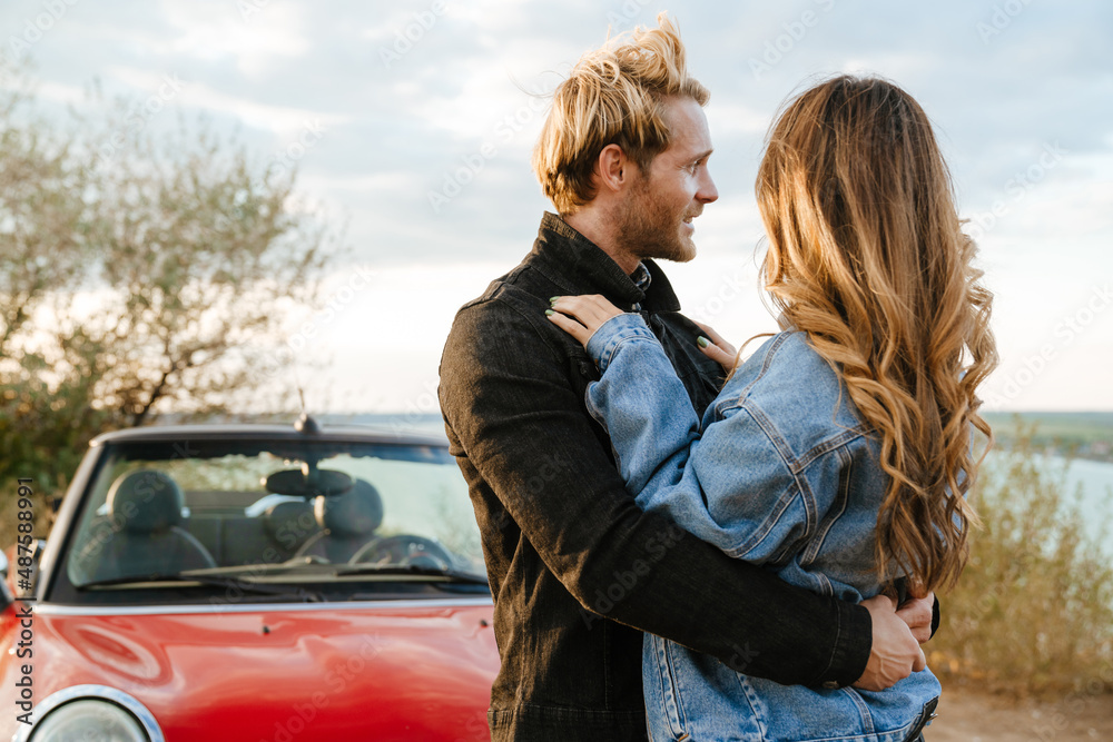 White couple smiling and hugging while standing by car during trip