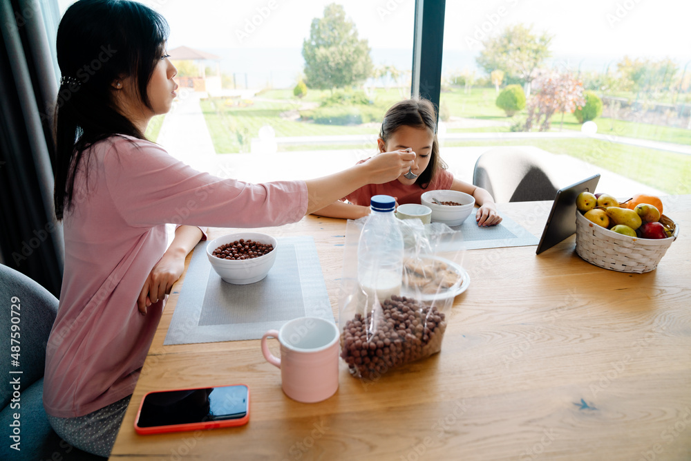 Asian girl using tablet computer while having breakfast with her mother Asian girl using tablet computer while having breakfast with her mother