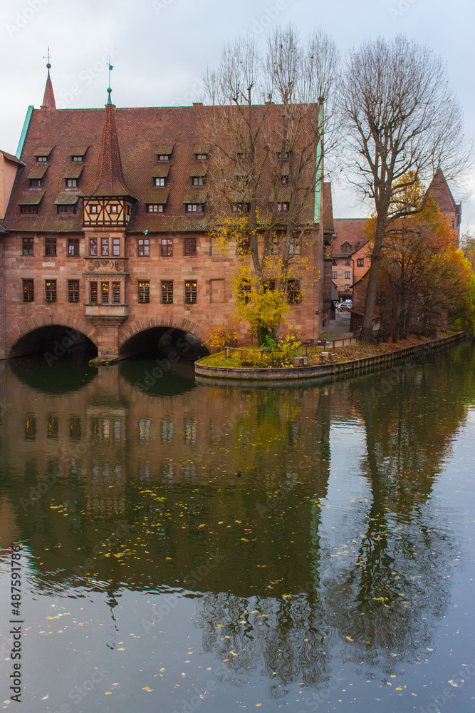 Fototapeta premium Nuremberg landmark. Medieval hospital museum house over canal. Old town of Nuremberg, Germany. Tranquil autumn landscape in old town. Fall season in historical downtown.