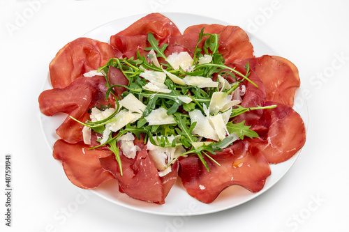 Plate of bresaola with rocket and parmesan in close-up on a white background. Typical Italian food. photo