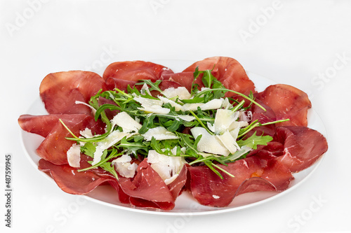 Plate of bresaola with rocket and parmesan in close-up on a white background. Typical Italian food.