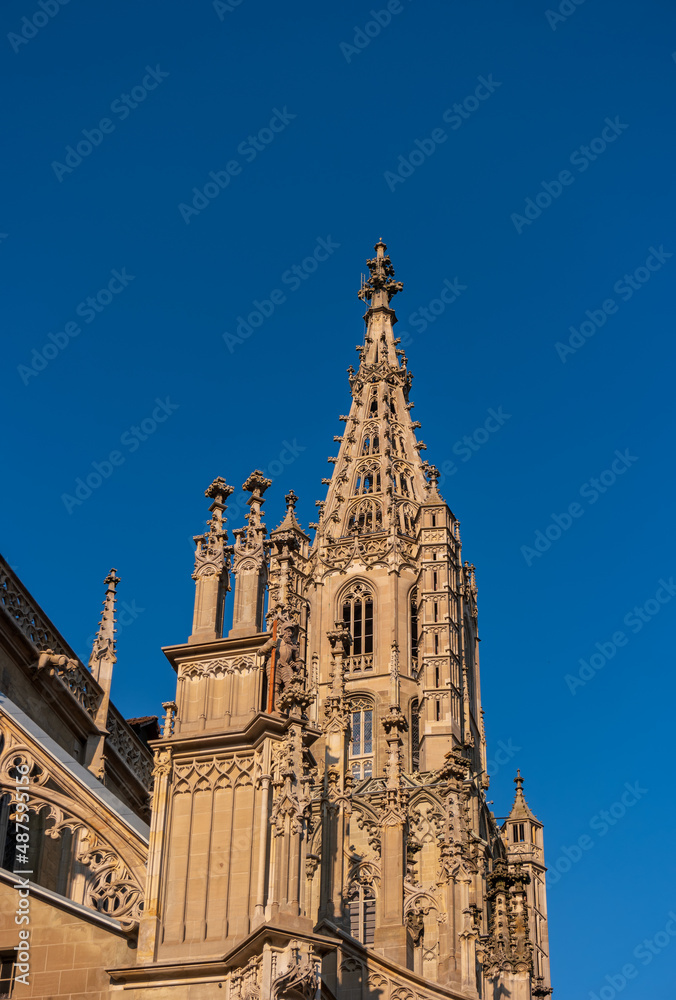 The ornate gothic bell tower of Bern Minster against a blue sky, Switzerland.