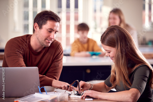 Father Helps Teenage Daughter With Electronics Project Sitting At Kitchen Table At Home With Laptop