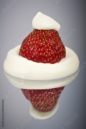 Whipped frozen yogurt or cream on strawberries. Close-up with reflection on a mirror surface.