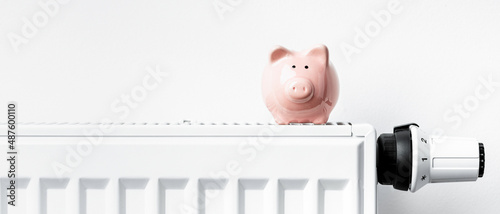 Sparschwein steht auf Heizkörper mit Thermostat - Banner #487600110