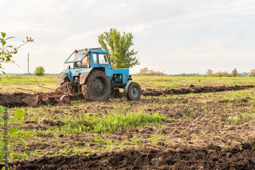 Old blue tractor on the field working. Farmer plowing stubble field in tractor preparing plows the land, agricultural works at farmlands, agriculture tractor-landscape. Tractor Plowing. Old blue tractor on the field working. Farmer plowing stubble field in tractor preparing plows the land, agricultural works at farmlands, agriculture tractor-landscape. Tractor Plowing.