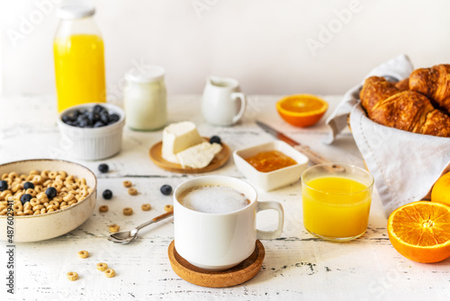 Breakfast concept with cup of coffee, croissants, wholegrain hoops, milk, orange juice, yogurt and blueberries