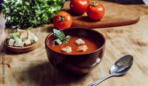 Fotografie tomato soup in a brown plate stands on a wooden background, rustic