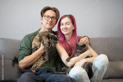 a man and a woman sit on a gray sofa and hug cats