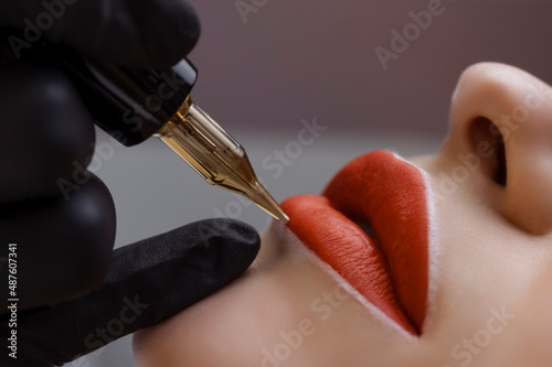 Cosmetologist makes permanent makeup on a woman's face. Specialist applies a tattoo on the patient's lips close-up