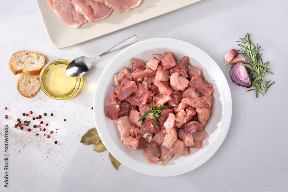 Composition with diced raw poultry, pork meat, oil, herbs on white background, top view. Meat in cubes on a white plate. Composition with diced raw poultry, pork meat, oil, herbs on white background, top view. Meat in cubes on a white plate.