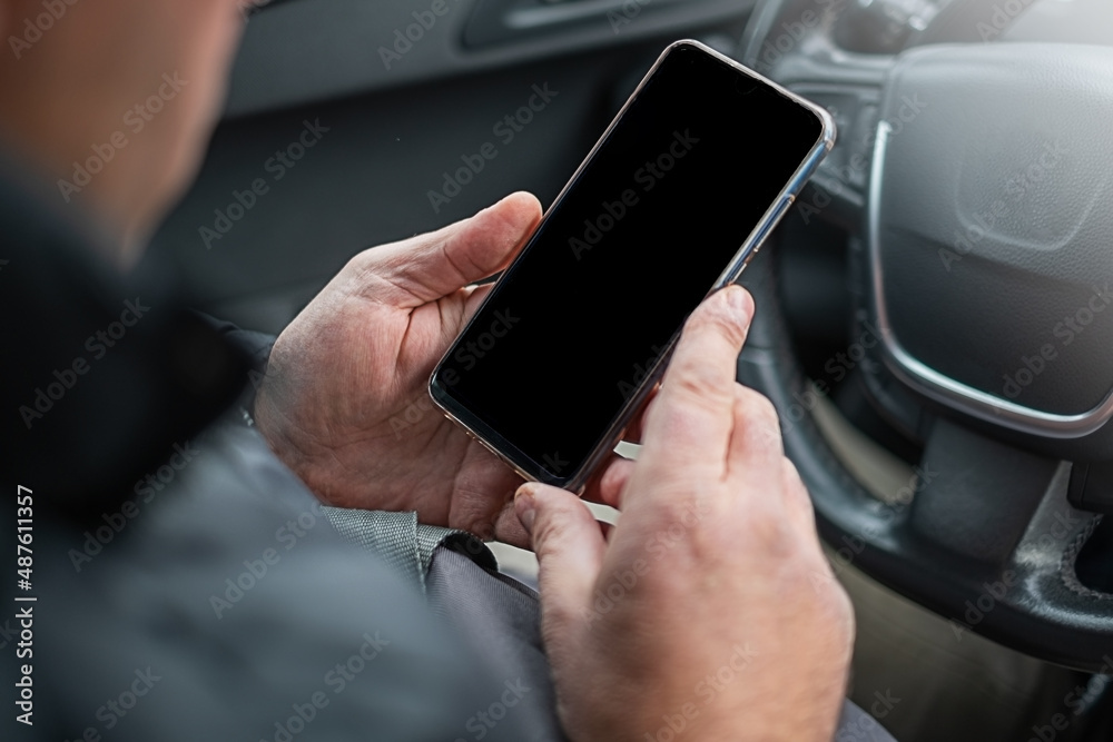 Male hands holding smartphone behind the wheel on the car