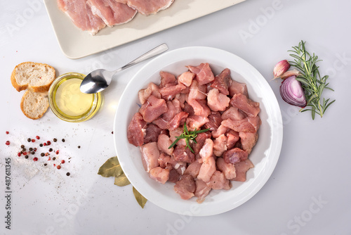 Composition with diced raw poultry, pork meat, oil, herbs on white background, top view. Meat in cubes on a white plate.