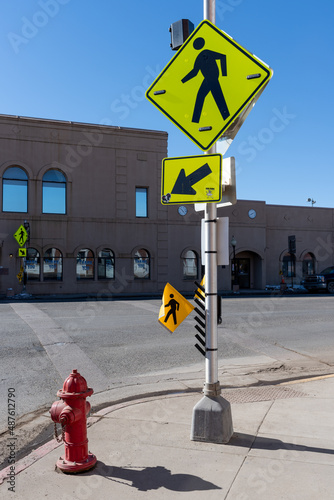 A bright yellow crosswalk sign with a black figure of a pedestrian, a yellow sign with an arrow and a yellow flag to be carried while crossing the street.