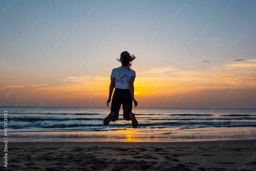 Unrecognizable young woman jumping on the beach at sunset