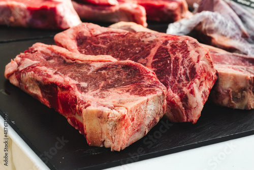 Big chunky raw cuts of beef steaks on a black marble slate