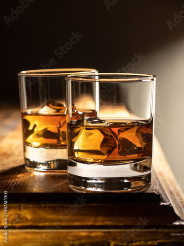 Two glasses of whisky on the rocks on a wooden bartop