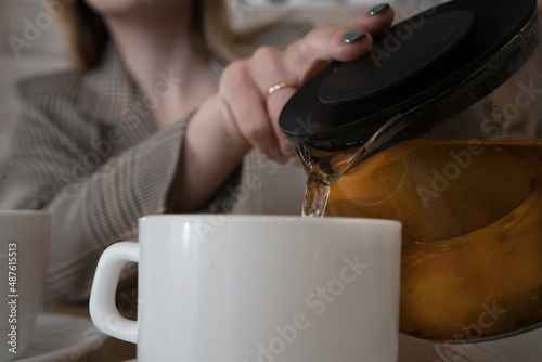 married woman pouring a cup of tea in a cafe in a white mug