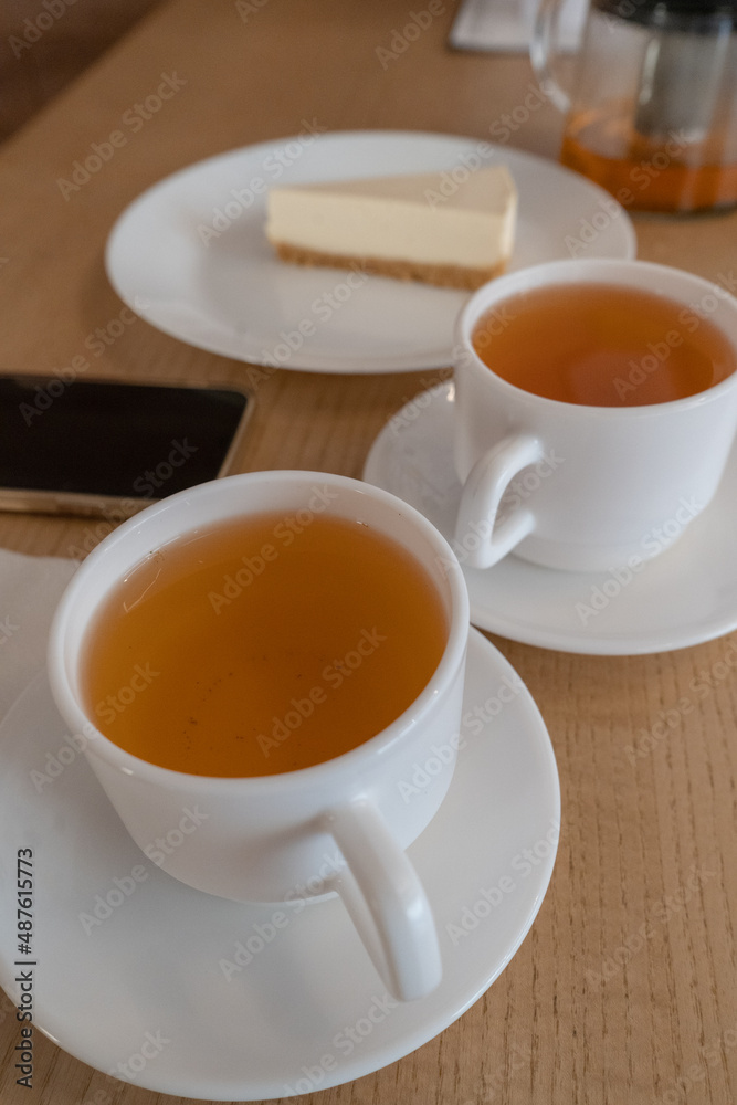 two cups of tea and a cheesecake cake a girl's hand with a phone in her hands in a cafe daylight lunch lunch snack two cups of tea and a cheesecake cake a girl's hand with a phone in her hands in a cafe daylight lunch lunch snack