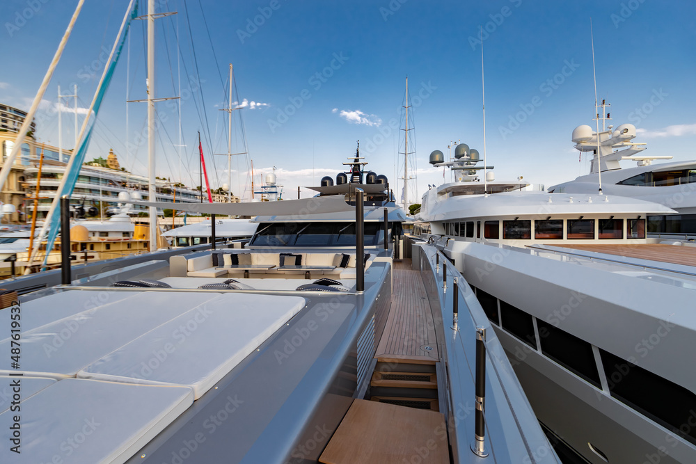 Fototapeta premium The front deck of huge yacht in port of Monaco at sunset, the place for landing of helicopter, a lot of motorboats are on background, the chrome plated handrail, megayacht is moored in marina, dusk