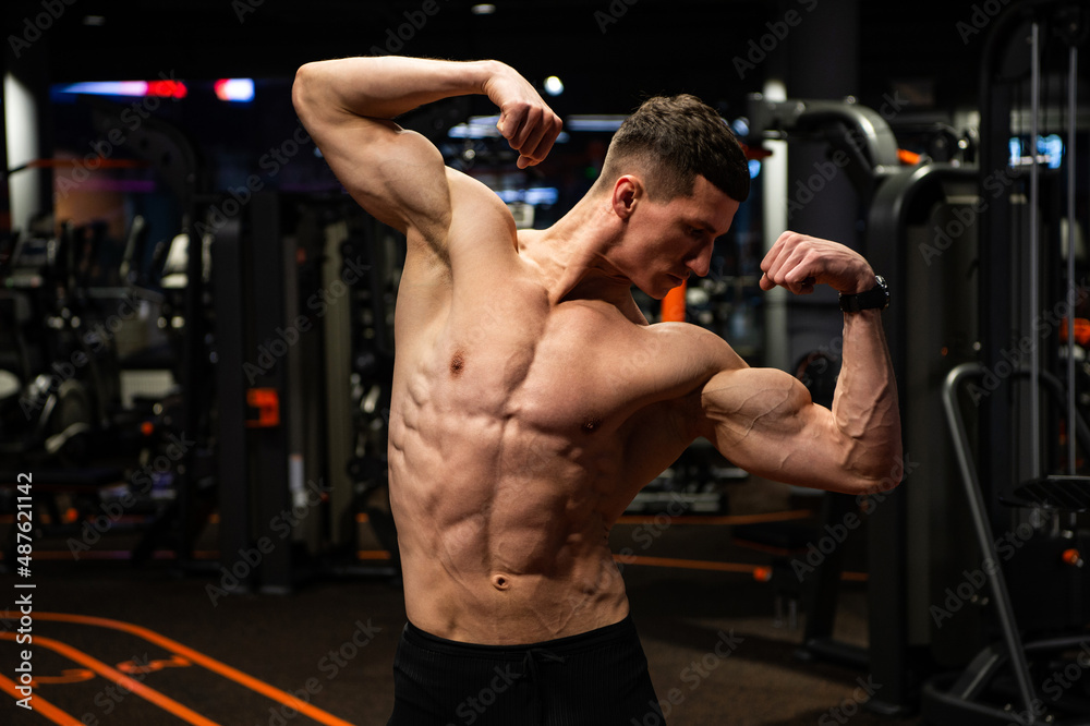 Strong guy with fit torso flexing arms muscles standing in double biceps pose in gym, strength Strong guy with fit torso flexing arms muscles standing in double biceps pose in gym, strength