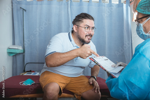 An upset male patient in his 30s argues and contests the bad diagnosis of a physician. In denial or disbelief. At the ER ward of a hospital. photo