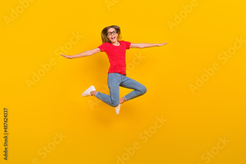 Full length photo of young excited lovely girl jump arms balance airplane isolated over yellow color background