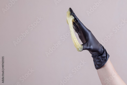 Shugaring. Sugar paste in hand. Hair removal with hot wax. Woman's hand in a medical black glove holds yellow sugar paste or wax for depilation. Close-up. Space for text.