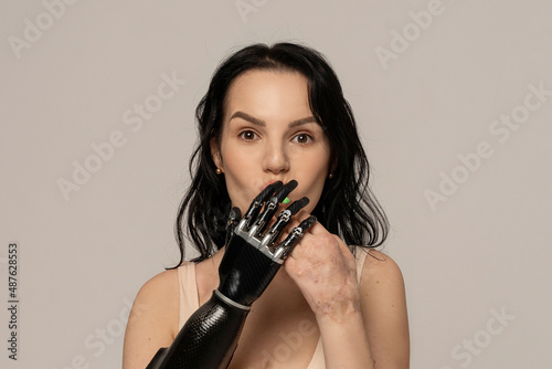 Obraz na płótnie Beauty disabled Woman closing mouth by bionic arm, artificial hand isolated on beige background