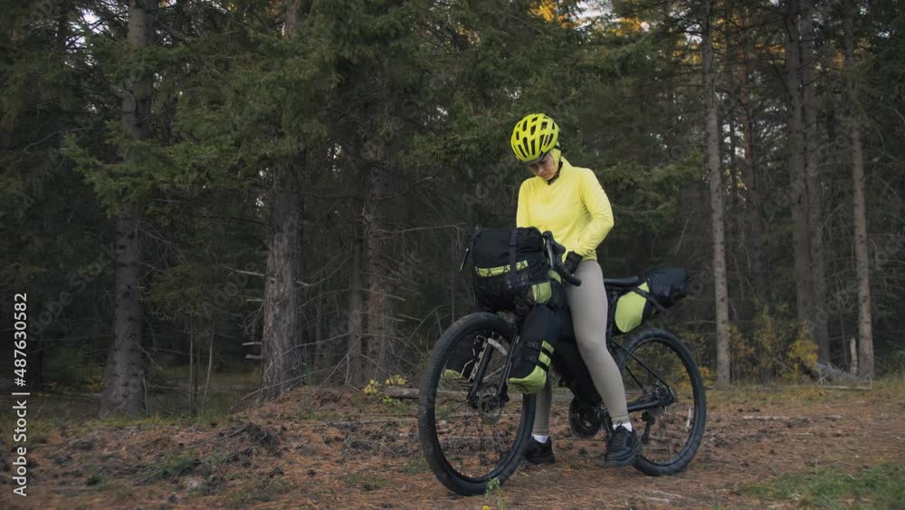 The woman travel on mixed terrain cycle touring with bike bikepacking outdoor. The traveler journey with bicycle bags. Stylish bikepacking, bike, sportswear in green black colors. Magic forest park. The woman travel on mixed terrain cycle touring with bike bikepacking outdoor. The traveler journey with bicycle bags. Stylish bikepacking, bike, sportswear in green black colors. Magic forest park.