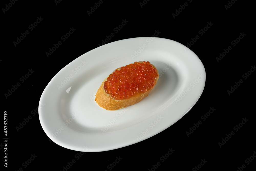 Red caviar on a piece of bread on a white plate isolated on a black background Red caviar on a piece of bread on a white plate isolated on a black background