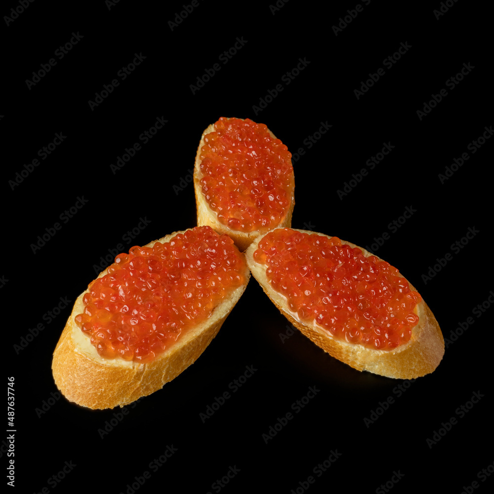 Red caviar on a piece of bread isolated on a black background