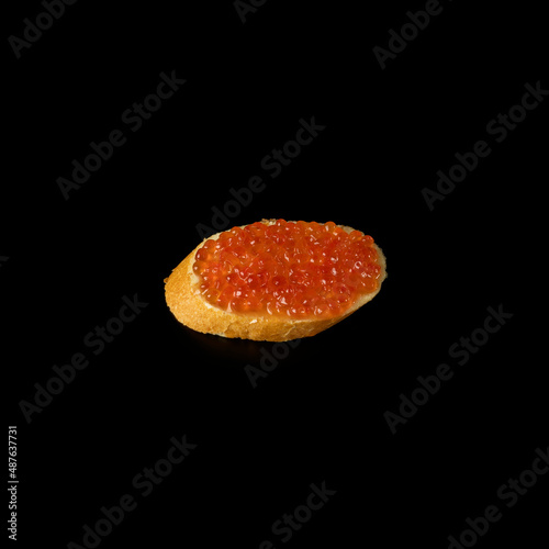 Red caviar on a piece of bread isolated on a black background