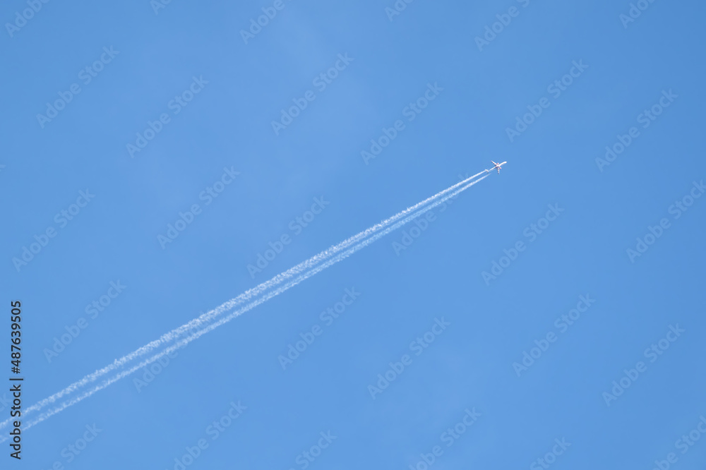 Distant passenger jet plane flying on high altitude on clear blue sky leaving white smoke trace of contrail behind. Air transportation concept Distant passenger jet plane flying on high altitude on clear blue sky leaving white smoke trace of contrail behind. Air transportation concept