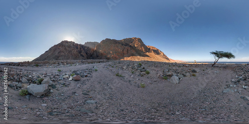 full seamless spherical hdri 360 panorama view of sunset in desert near tree with sun shines from behind the mountain on coast of sea in equirectangular projection, ready for VR AR virtual reality