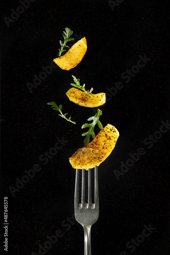 A slice of fried potatoes on a fork and flying potatoes and arugula on a black background.