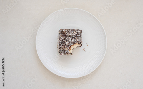 High angle view of partly eaten lamington cake on white plate with crumbs (selective focus) photo