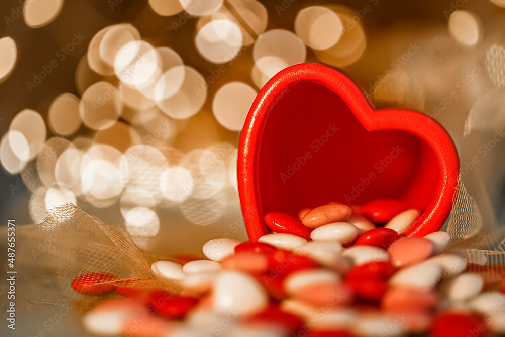 A red vase and heart shaped glazed chocolates are on the table. Blurred background with yellow bokeh.