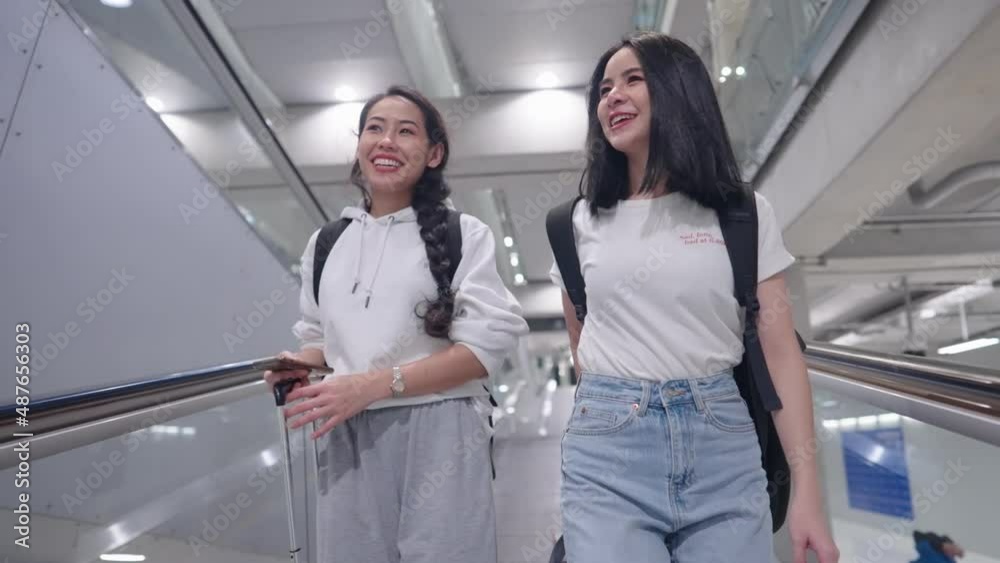 Attractive young asian happy friends traveling with suitcase backpack walking talking on escalator walkway, vacation travel abroad, best friends having fun discussing together, air traveling concept Attractive young asian happy friends traveling with suitcase backpack walking talking on escalator walkway, vacation travel abroad, best friends having fun discussing together, air traveling concept