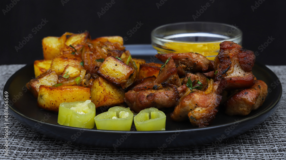 Pieces of fried pork with onions and herbs, rustic potatoes, green pepper slices and mustard sauce in the background. Shallow depth of field