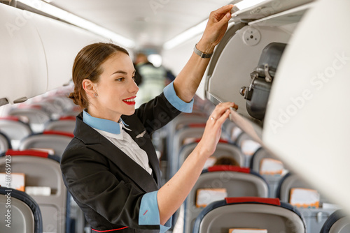 Joyful stewardess checking overhead luggage bin in airplane photo