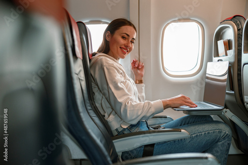 Cheerful young woman using notebook in airplane